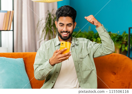 Indian Arabian young man at home use smartphone celebrating success victory winning play online game 115506116