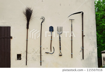 On the wall of the shed hangs a set of gardening tools. 115507016
