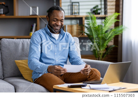 Cheerful man sitting on a sofa at home, reading a document, and smiling with a laptop nearby. Cheerful man sitting on a sofa at home, reading a document, and smiling with a laptop nearby. 115507303