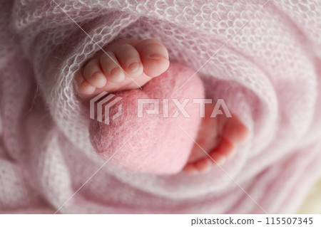 The tiny foot of a newborn baby. Soft feet of a new born in a wool pink blanket. Closeup of toes, heels and feet of a newborn. Knitted pink heart in the legs of baby. Macro studio photography.  115507345