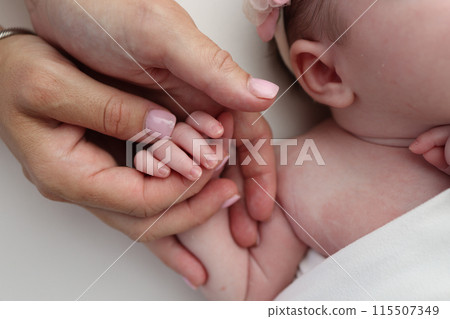 Small hand of a newborn baby with tiny fingers, head, nose and ear of a newborn. Palm hand of parents, father and mother of a newborn. Studio macro photography. Small hand of a newborn baby with tiny fingers, head, nose and ear of a newborn. Palm hand of parents, father and mother of a newborn. Studio macro photography. 115507349