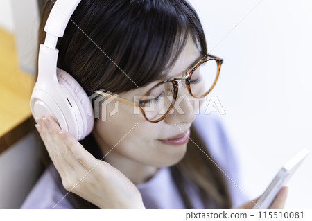 A woman wearing glasses listening to music on her smartphone through headphones 115510081