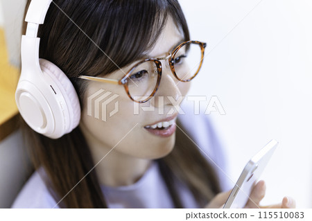 A woman wearing glasses listening to music on her smartphone through headphones 115510083