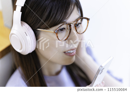A woman wearing glasses listening to music on her smartphone through headphones 115510084