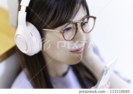A woman wearing glasses listening to music on her smartphone through headphones 115510085