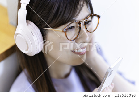 A woman wearing glasses listening to music on her smartphone through headphones 115510086