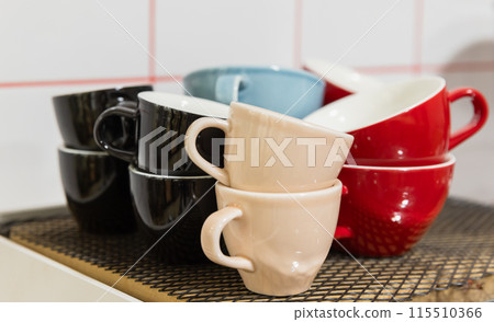 Set of bright ceramic cups stand in front of white wall Set of bright ceramic cups stand in front of white wall 115510366