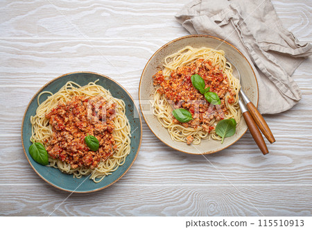 Two plates of spaghetti bolognese with basil on wooden table 115510913