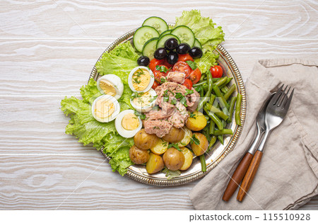 Nicoise salad with tuna, eggs, potatoes, green beans, and olives on a white table 115510928