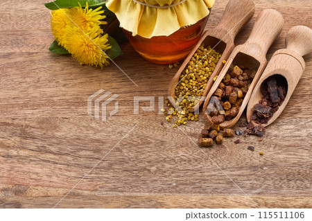 A jar of honey with fabric lid, pollen granules, beebread, and dandelion flowers 115511106