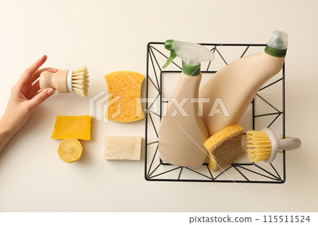 Bottles with detergent in basket, soap, brushes in hand and sponges on beige background, top view Bottles with detergent in basket, soap, brushes in hand and sponges on beige background, top view 115511524