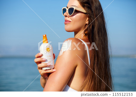 Woman putting sunblock lotion on shoulder before tanning during summer holiday on beach. Sun cream. Suntan. Beautiful Woman Applying Sunscreen Solar Cream. Skin care. Sun protection Woman putting sunblock lotion on shoulder before tanning during summer holiday on beach. Sun cream. Suntan. Beautiful Woman Applying Sunscreen Solar Cream. Skin care. Sun protection 115512153