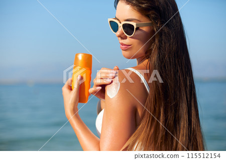 Beautiful Woman in Bikini Applying Sun Cream on Tanned Shoulder. Sun Protection. Skin and Body Care. Girl Using Sunscreen to Skin. Portrait Of Female Holding Suntan Lotion and Moisturizing Sunblock. Beautiful Woman in Bikini Applying Sun Cream on Tanned Shoulder. Sun Protection. Skin and Body Care. Girl Using Sunscreen to Skin. Portrait Of Female Holding Suntan Lotion and Moisturizing Sunblock. 115512154