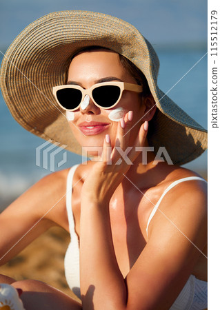 Beautiful young woman with sun cream on face. Girl holding sunscreen bottle on the beach and applying moisturizing lotion on skin.Skin care. Sun protection. Suntan Beautiful young woman with sun cream on face. Girl holding sunscreen bottle on the beach and applying moisturizing lotion on skin.Skin care. Sun protection. Suntan 115512179