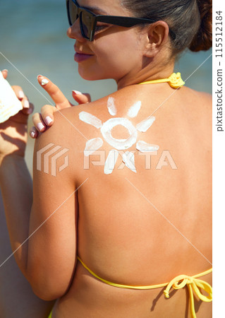 Woman Applying Sun Cream on Tanned Shoulder In Form Of The Sun. Sun Protection.Sun Cream. Skin and Body Care. Girl Using Sunscreen to Skin. Female Holding Suntan Lotion and Moisturizing Sunblock. 115512184