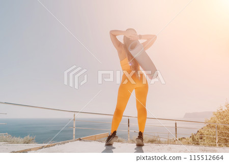 Fitness woman sea. Happy middle aged woman in orange sportswear exercises morning outdoors on yoga mat with laptop in park over ocean beach. Female fitness pilates yoga routine. Healthy lifestyle. 115512664