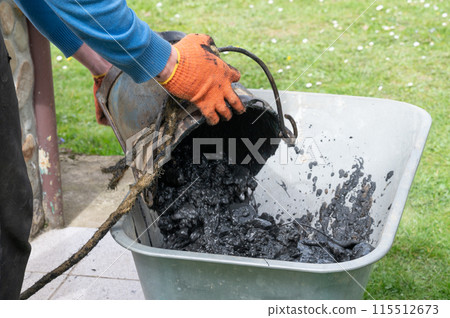A man pours mud from a bucket into a wheelbarrow from the bottom of a well. 115512673