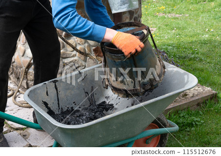 A man pours mud from a bucket into a wheelbarrow from the bottom of a well. 115512676