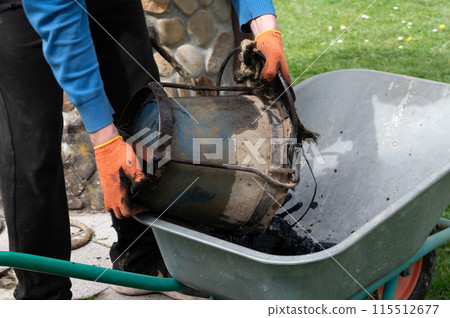 A man pours mud from a bucket into a wheelbarrow from the bottom of a well. 115512677