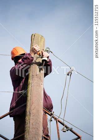 A male electrical worker repairs an electrical transmission line. A male electrical worker repairs an electrical transmission line. 115512715