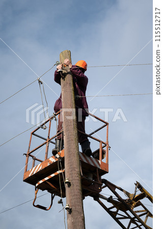 A male electrical worker repairs an electrical transmission line. A male electrical worker repairs an electrical transmission line. 115512717