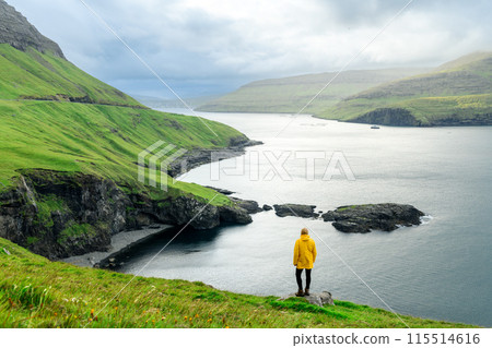 Lonely tourist standing on edge of the cliff on Vagar island Lonely tourist standing on edge of the cliff on Vagar island 115514616