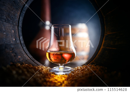 Tasting glass with whiskey standing inside of old oak barrel 115514628