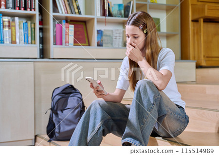 Sad teenage girl student looking at smartphone screen inside high school classroom 115514989
