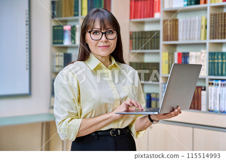 Middle aged elegant woman using laptop inside library Middle aged elegant woman using laptop inside library 115514993