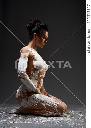 Woman Kneeling In White Clay Against a Dark Background Woman Kneeling In White Clay Against a Dark Background 115515137