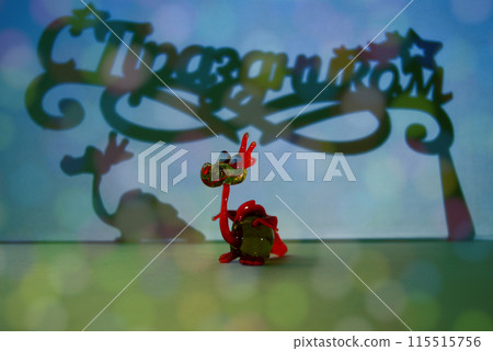 A toy dragon, its shadow and a shadow with an inscription. A little dragon and a congratulatory inscription Happy Holidays in Russian. A toy dragon, its shadow and a shadow with an inscription. A little dragon and a congratulatory inscription Happy Holidays in Russian. 115515756