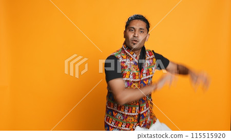 Ecstatic person wearing traditional indian attire doing energetic dance steps. Lively talented man doing entertaining bollywood choreography moves, studio background, camera B 115515920