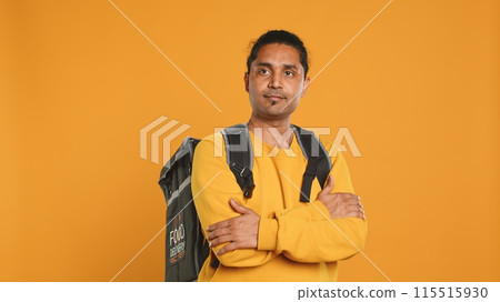 Portrait of man holding thermal backpack, crossing arms, ready to fulfill orders, studio backdrop. Calm food delivery service worker prepared to do delivery to customers, camera A Portrait of man holding thermal backpack, crossing arms, ready to fulfill orders, studio backdrop. Calm food delivery service worker prepared to do delivery to customers, camera A 115515930