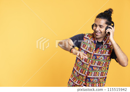 Happy indian person wearing headphones having fun, dancing on rhythm, enjoying leisure time. Cheerful man entertaining himself doing funky movements on tunes, isolated over studio background Happy indian person wearing headphones having fun, dancing on rhythm, enjoying leisure time. Cheerful man entertaining himself doing funky movements on tunes, isolated over studio background 115515942