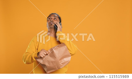 Delivery man arguing with customer on phone after arriving at destination and waiting for him, studio background. Indian person doing deliveries, scolding late client on telephone call, camera A 115515989