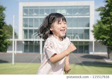 Smiling child (toddler) running on the grass. Running in front of a school building such as a park, nursery school, or kindergarten. Copy space available. Upper body. 115517636