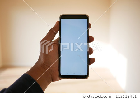 A person holding a smartphone with a blank screen in a welllit room, showing modern digital usage 115518411