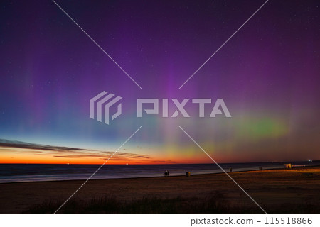 A mesmerizing aurora borealis display with vibrant purple, green, and blue hues over Jurmala beach in Latvia. The calm sea reflects the colors, enhancing the scene. 115518866