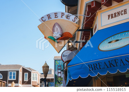 Close up view of a crepe shaped sign reading CREPES with seashell design, FRENCH sign below. European style architecture background, likely in San Francisco. 115518915