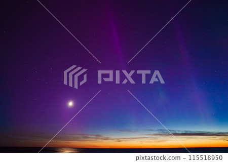 Vibrant aurora borealis illuminates the night sky near Riga and Jurmala, Latvia. The calm sea reflects hues of purple and blue, with a bright moon and setting sun. Vibrant aurora borealis illuminates the night sky near Riga and Jurmala, Latvia. The calm sea reflects hues of purple and blue, with a bright moon and setting sun. 115518950