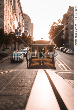 Iconic San Francisco cable car on Powell and Hyde Streets at sunset, passengers enjoying the ride. Classic architecture, golden light, authentic city scene. 115518988