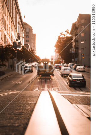Iconic San Francisco cable car moves along a bustling street at sunset, bathed in warm golden light. Urban beauty captured from street level perspective. Iconic San Francisco cable car moves along a bustling street at sunset, bathed in warm golden light. Urban beauty captured from street level perspective. 115518990