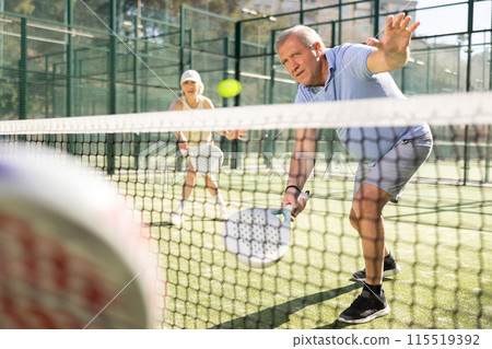 Determined sporty older man doing his best playing padel in court 115519392
