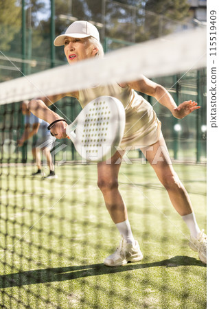 Motivated senior woman playing padel with her teammate in court Motivated senior woman playing padel with her teammate in court 115519409
