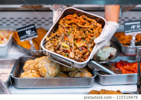 Salesman lays out a tray of pieces of lamb with noodles and vegetables on supermarket display window 115519478