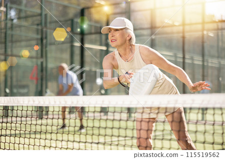 Determined sporty older woman doing her best playing padel in court 115519562