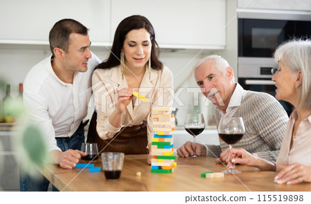 Joyful senior parents and young couple sitting around table playing brick game 115519898