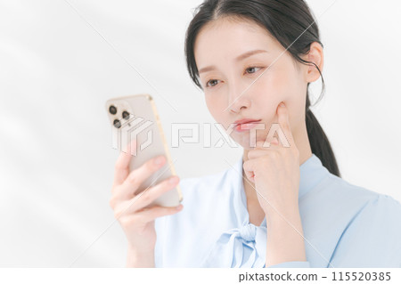 一位女士表情困惑地看著她的智慧型手機 一位女士表情困惑地看著她的智慧型手機 115520385