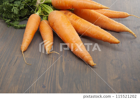 Bundle of vibrant orange carrots with green leafy tops on rustic table 115521202