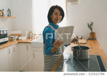 A woman in her 40s cooking while looking at a tablet A woman in her 40s cooking while looking at a tablet 115521790